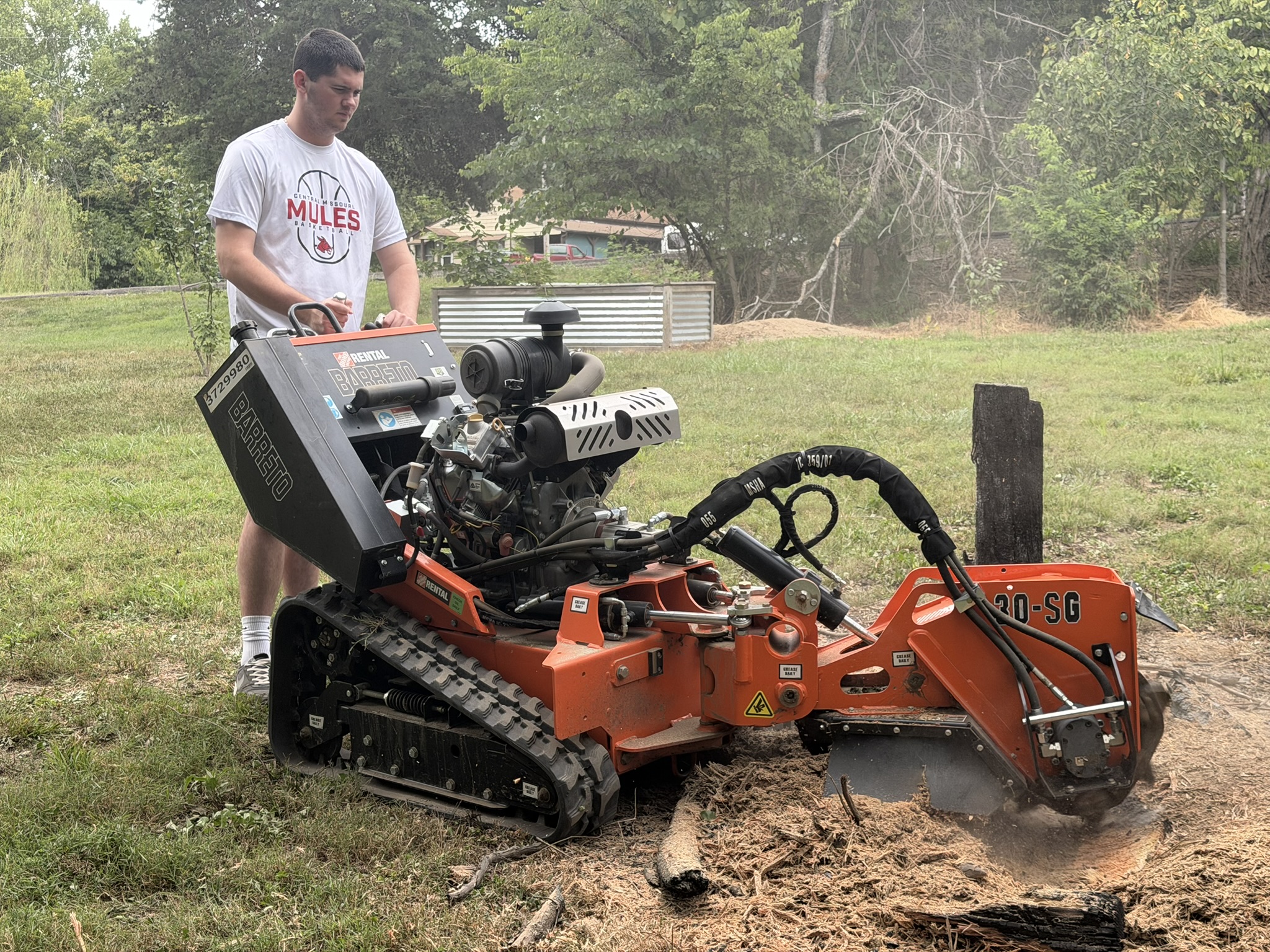 A crew member operating a stump grinder in a yard